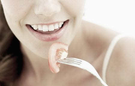 Woman holding a fork with a piece of tomato on it.