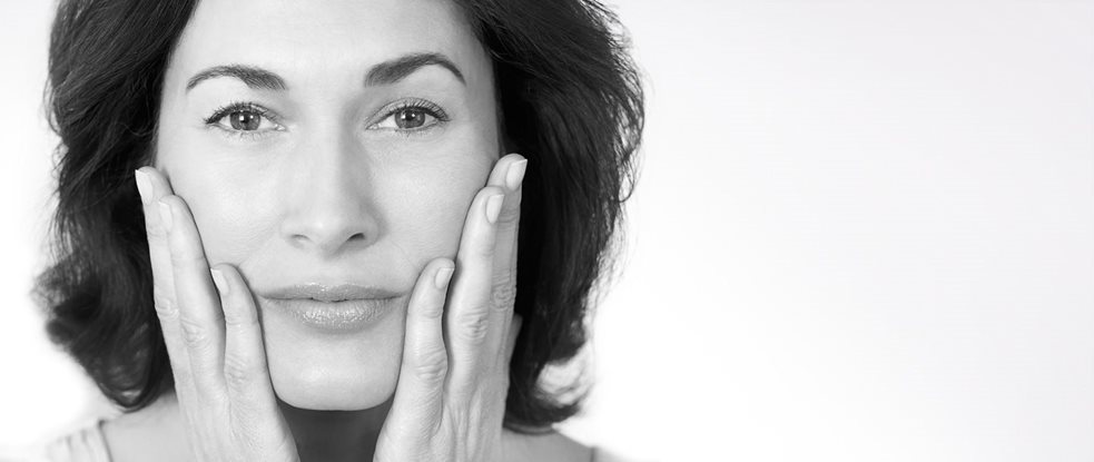 Middle-aged woman touching her cheeks with both hands.