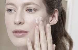 Woman applying cream on her left cheak.
