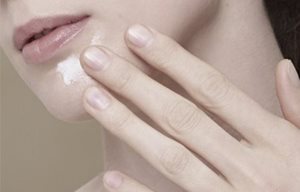 Woman applying cream on her chin.