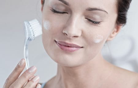 Woman cleansing her facial skin with a brush