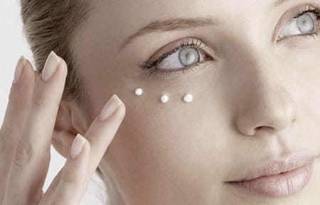 Woman applying cream for dry skin around the eyes